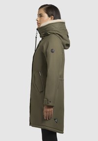 Olijfgroene parka met een nepbont gevoerde capuchon, voorzien van een ritssluiting aan de voorkant, zijzakken en een logopatch op de mouw.