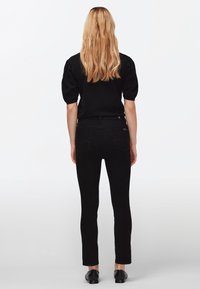 Černé slim džíny s klasickým pětikapsovým designem, vyrobené z denimu; zkombinované s černým trikem s krátkým rukávem a černými botami.