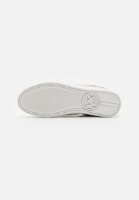 Semelle d'une basket blanche avec une accroche texturée, un logo circulaire portant les lettres "MK" et deux lignes parallèles près du talon sur un fond uni.