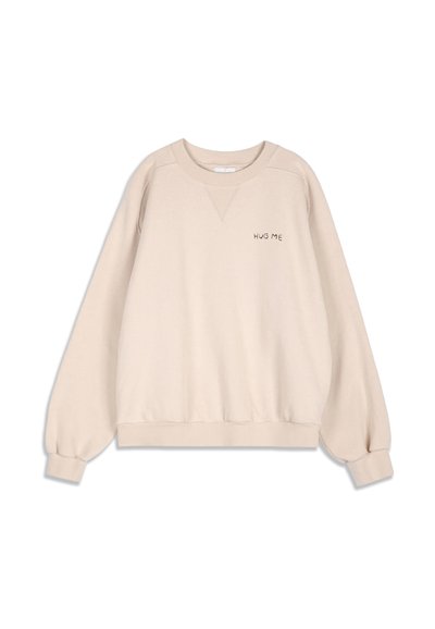 Sweat-shirt beige clair à col rond avec manches longues bouffantes et petit texte "HUG ME" sur la poitrine gauche.