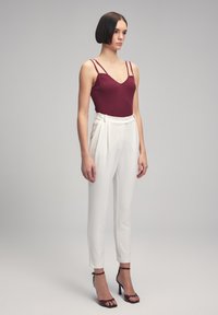 Burgundy ribbed bodysuit with thin straps, paired with high-waisted white pleated trousers and black ankle strap heels. Smooth textures.