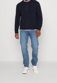 Jersey de punto marinero con cuello redondo, jeans de mezclilla azul y zapatillas blancas con detalles rojos. El jersey presenta puños y dobladillo acanalados.
