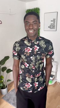 Camicia a maniche corte con bottoni caratterizzata da uno sfondo nero con vivaci motivi floreali in rosso, rosa e verde. Abbinata a pantaloni scuri.