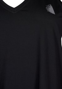 Czarny, sportowy top na ramiączkach z dekoltem w kształcie litery V. Wykonany z gładkiego materiału, z teksturowanym, paskowanym wcięciem w kształcie serca w kolorze białym.
