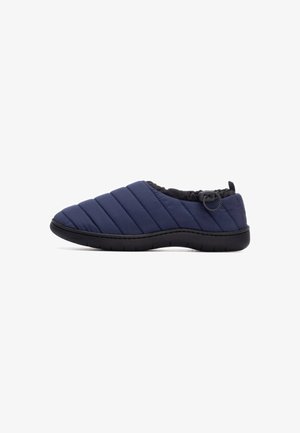 Zapato deslizable acolchado color marino con suela de goma negra. Cuenta con una abertura elástica negra recogida y un detalle decorativo de botón en el lateral.