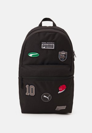 Sac à dos Puma noir avec plusieurs patches incluant des logos Puma, un ovale vert, le numéro 10, une casquette rouge et une icône de globe sur les poches avant.