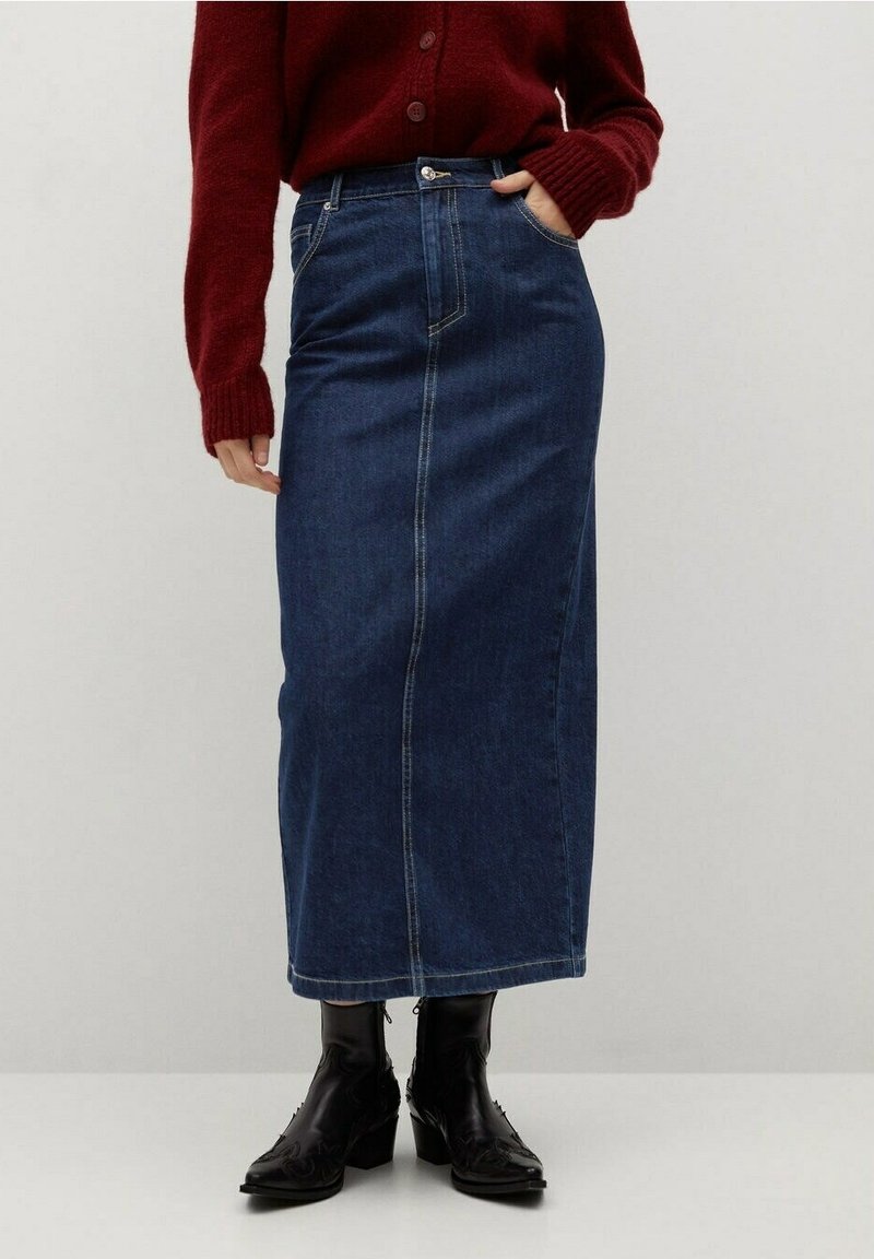 Tummansininen farkku maksihame, jossa on suora leikkaus, etutaskut ja näkyvät ompeleet. Yhdistetty mustiin korkokenkiin.