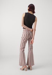 Femme aux cheveux courts et foncés portant un haut sans manches noir, un pantalon à rayures verticales multicolores taille haute et des sandales à talons beiges.