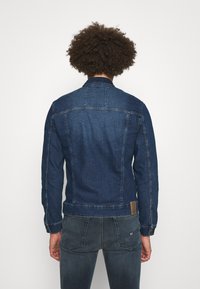 Jeansjacke, dunkelblau, klassischer Kragen, lange Ärmel, gepunktete Manschetten, Schulterpasse, Saum mit dezentem Branding-Patch, glatte Textur.