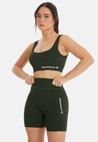 Completo sportivo verde scuro composto da un reggiseno a coste e pantaloni corti a vita alta, entrambi con il logo bianco "SQUATPROOF" sul davanti.