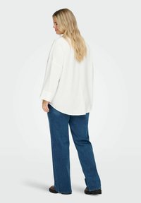 Maglietta bianca a vestibilità ampia con maniche lunghe e polsini a coste, abbinata a jeans denim blu a gamba dritta. Design semplice e pulito.