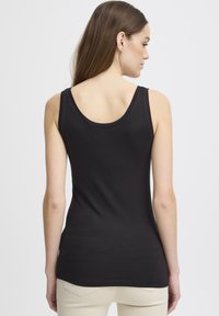 Svart ermeløs topp med scoop hals, glatt tekstur og en tettsittende design, kombinert med lyse bukser og minimalistisch stil.