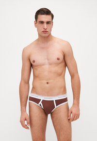 Chiloți din bumbac maro cu accente albe, având un brâu cu marcă și o potrivire strânsă. Țesătura are o textură netedă și un design minimalist.