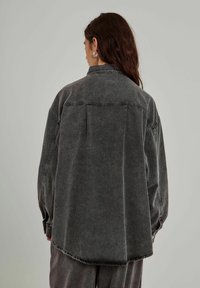 Übergroßes dunkelgraues Denim-Hemd mit spitzem Kragen, langen Ärmeln und einem einzigartigen Schulterlinien-Detail auf der Rückseite.
