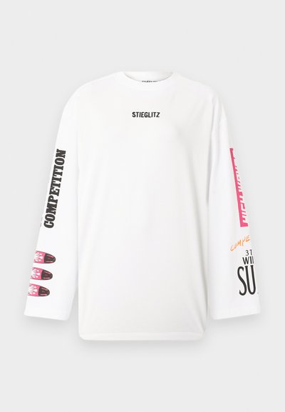Λευκό πουκάμισο με μακριά μανίκια με το κείμενο "STIEGLITZ" στο στήθος, "COMPETITION" στο αριστερό μανίκι και πολύχρωμο γραφικό και κείμενο στο δεξί μανίκι.