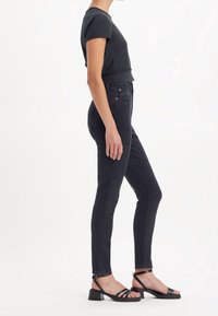 Jeans ajustados negros con cintura alta y piernas estrechas, combinados con una blusa oscura de manga corta y sandalias negras de tacón bloque con tiras.