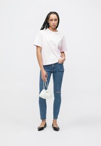 Ανοιχτό ροζ βαμβακερό T-shirt με κοντά μανίκια και άνετη γραμμή, συνδυασμένο με εφαρμοστά μπλε τζιν με ελαφριά φθορά. Μικρή λευκή τσάντα.