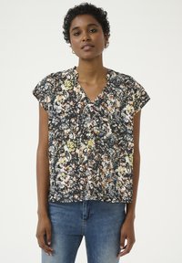 Blomstret kortærmet bluse i sort, creme og lyse farver med V-hals og afslappet pasform; har en tekstureret overflade og knapdetaljer.