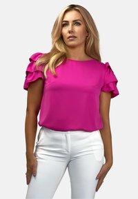 Fuksjowa bluzka z krótkimi, falbaniastymi rękawami i okrągłym dekoltem, w połączeniu z białymi, dopasowanymi spodniami. Gładki materiał, swobodny krój.