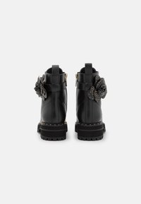 Botas de cuero negras hasta el tobillo con suela gruesa, cremallera lateral y un acento decorativo de flor con tachuelas. Textura suave y forma redondeada.