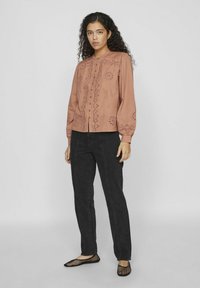 Blusa de color rosa con detalles bordados y cierre de botones; combinada con jeans negros y bailarinas de malla. Mangas largas con puños fruncidos.
