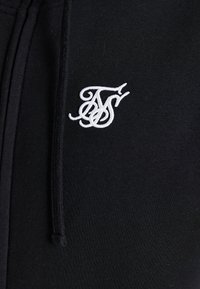 Black sweatpants with a soft texture, featuring a white embroidered logo on the left side and drawstring at the waist.