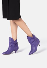 Paarse leren enkelboots met een spitse neus, geplooide details en een lage kittenhak. Gladde textuur, modern design.