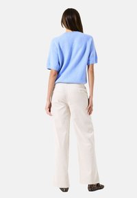 Un pull bleu clair à manches courtes associé à un pantalon large crème. Le pull a une texture douce ; le pantalon a une coupe droite et dispose de poches arrière.