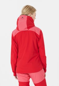 Veste rouge avec des accents roses, capuche et manches longues. Fabriquée à partir d'un matériau léger avec une texture lisse. Elle présente un logo au dos.