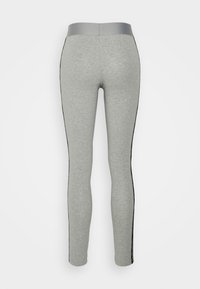 Leggings grises hechos de una tela suave y elástica, con una cinturilla ancha y lisa, y franjas laterales negras, de diseño ajustado y estrechado.
