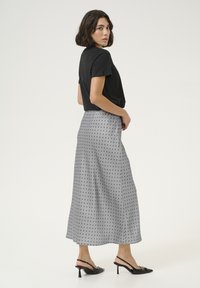 Camiseta negra, falda midi gris con lunares negros, textura suave, hasta los tobillos, con tacones negros de tiras. Modelo de perfil.