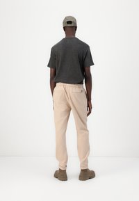 T-shirt noir à manches courtes, pantalon beige à taille élastique et bottines brunes à cheville. Design simple avec une texture subtile, vu de dos.