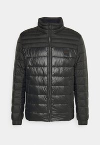 Giacca nera imbottita con colletto alto, design trapuntato orizzontale, zip frontale e patch con logo sul lato sinistro del petto. Tessuto liscio e lucido.