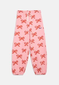 Rosa Trainingshose mit einem Muster aus roten Schleifen. Elastischer Bund mit Kordelzug, geraffte Bündchen und ein kleines blaues "Tiny"-Logo an der Seite.
