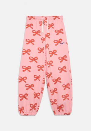 Rožinės treningo kelnės su raudonų lankų raštu. Elastingas liemuo su virvute, gather'un kūno rankogaliai ir mažas mėlynas "Tiny" logotipas šone.