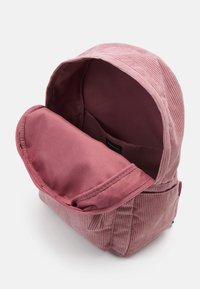 Petit sac à dos en velours côtelé rose avec compartiment principal ouvert montrant la doublure intérieure et une poche latérale sur un fond blanc.