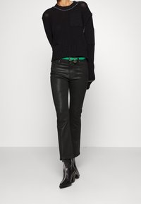 Suéter negro de punto con parches texturizados, cinturón verde, pantalones de cuero brillantes negros y botas de tacón negras con acentos blancos.