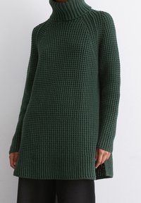 Grüner gestrickter Rollkragenpullover mit strukturiertem Muster, langen Ärmeln und seitlichen Schlitzen. Der Stoff scheint weich und schwer zu sein.