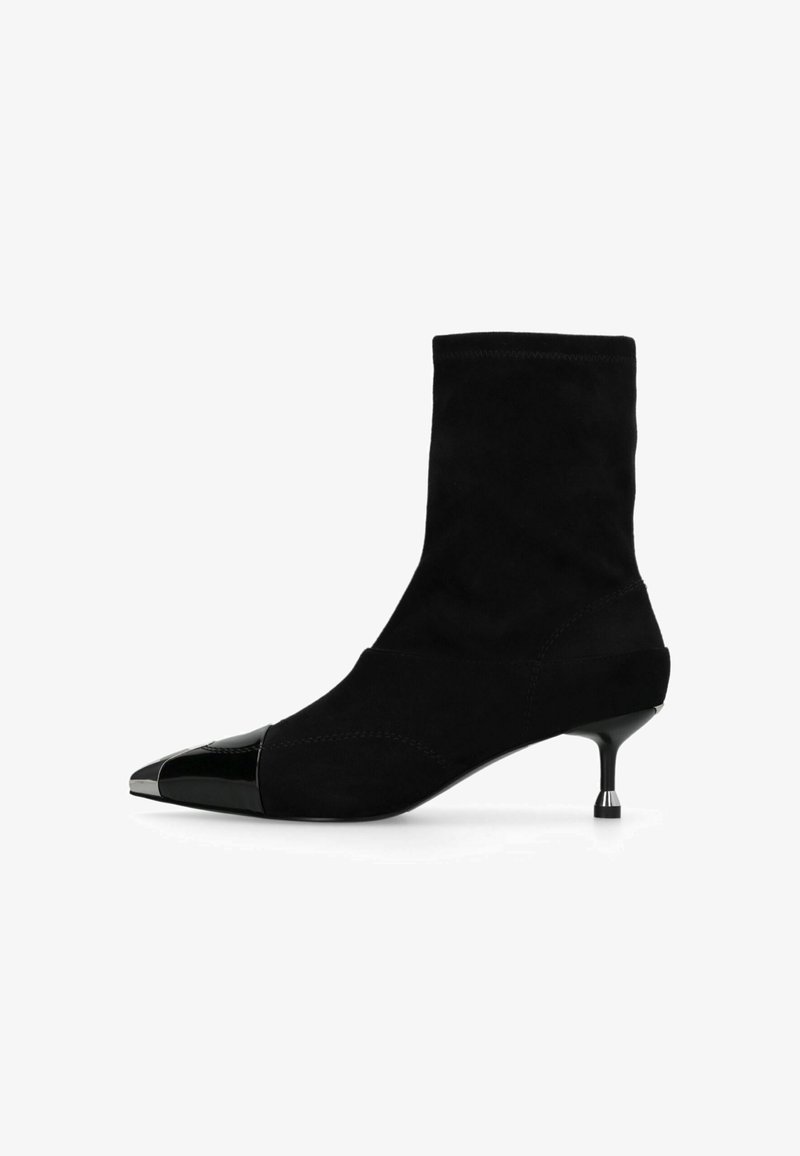 Bottine noire à cheville avec embout métallique pointu et petit talon fin sur fond blanc.