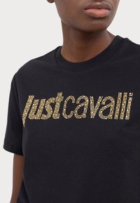 Czarna bawełniana koszulka z teksturowanym złotym wzorem z cyrkoniami, z wyraźnym napisem "justcavalli" na przodzie.