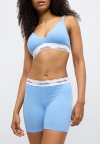 Ανοιχτό γαλάζιο bralette Calvin Klein με λαιμόκοψη σε σχήμα V, ρυθμιζόμενες τιράντες και λευκή ριγέ ζώνη με το λογότυπο. Ταιριαστό μπλε σορτς με παρόμοια ζώνη.