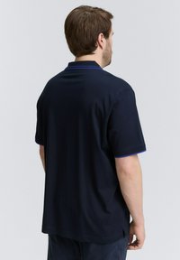 Navyblauwe polo met korte mouwen, voorzien van een kraag en contrasterende paarse accenten op de mouwranden, met een gladde textuur.