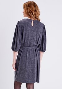 Vestido de jersey gris con un escote en forma de ojal en la parte posterior, mangas cortas y abullonadas, y detalle de cintura fruncida. Textura suave y diseño hasta la rodilla.