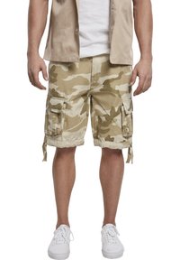 Beige camouflage cargoshorts med flera fickor, dragsko på sidorna och en avslappnad passform, kombinerade med en vit t-shirt och vita sneakers.