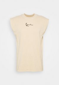 Beige ermeløs T-skjorte med rund hals, med en svart logo i kursiv tekst foran og en avslappet passform.