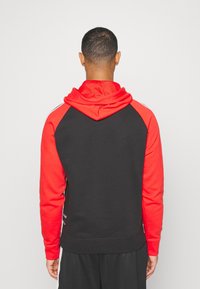 Felpa con cappuccio nera e rossa con maniche raglan, caratterizzata da un cappuccio testurizzato e un dettaglio a strisce laterali minimal. Realizzata in tessuto morbido.