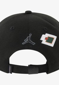Svart caps med buet skygge. Har en grå brodert Jumpman-logo og et rektangulært merke med grønne og oransje detaljer på siden.