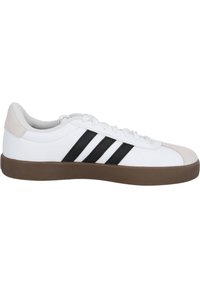 Scarpa da ginnastica bianca con tre strisce nere, dettagli beige sul tallone e sulla punta, e una suola in gomma marrone. Materiale liscio e design classico.