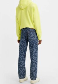 Sudadera amarilla clara con un diseño corto, combinada con jeans azul oscuro con un patrón en espiral. Zapatillas completan el conjunto.