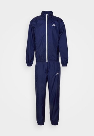 Navyblauwe waterdichte trainingsoutfit met een jasje met volledige ritssluiting en hoge kraag, en broek met elastische taille, versierd met een witte logoaccent.